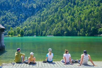 Sch&ouml;ner Blick auf den K&ouml;nigssee, mit Touristen, die ihre F&uuml;sse ins Wasser halten. In Bayern, Deutschland.