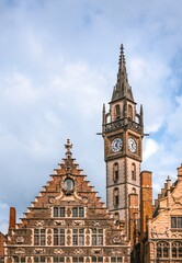 Obraz premium The magnificent clock tower of the old post office in Ghent, Belgium, towers high above the elegant facade of a beautiful historic house in the city center.