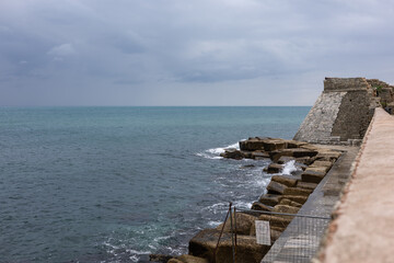 ancient stone bastion and defensive sea wall overlooking the turquoise ocean under a dramatic cloudy sky, historic coastal fortification and rocky shoreline