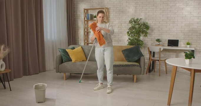 Woman prepares a mop for cleaning in a modern cozy living room with a couch and plants.