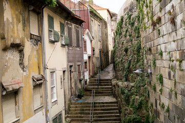 High-angle shot of a classic European cobblestone street featuring historic buildings, stone stairs, and lush green moss on ancient walls.