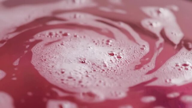 Close up of pink bath bomb fizzing and swirling in water creating foam bubbles.