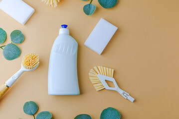 White bottle with cleaning brushes and sponges, natural green leaves, simple home cleaning supplies...