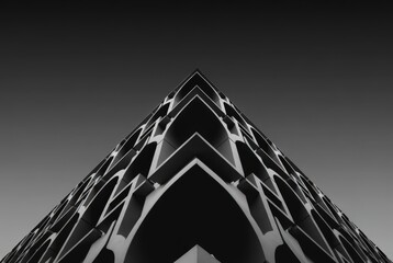 The structure shows a unique architectural design with a sharp point facing skyward. The contrast of dark and light highlights the patterns in the building's facade