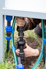 Hands connecting a water filter to a system of pipes and hoses for an automatic drip irrigation system.