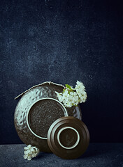An arrangement of black handcrafted ceramic with white cherry blossoms. Still life. Copy space. Black stone background