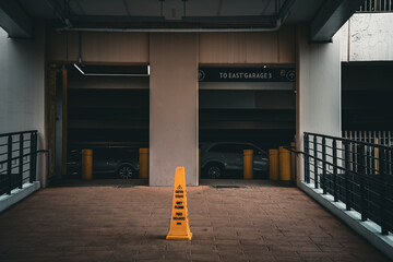 Yellow caution cone warns of wet floor in a dimly lit parking garage with cars © Tom
