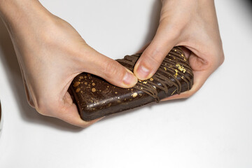 A hand holds a piece of luxurious Dubai chocolate covered in dark chocolate and decorated with edible gold flakes. The rich texture and golden accents highlight the premium quality desert
