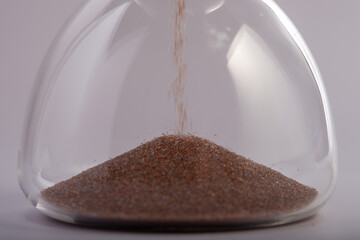 Hourglass sand timer glass clock on white background with flowing brown sand. Concept for time management, deadline pressure, business planning, and measuring duration in a minimalist studio setting