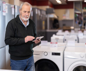 Eldery man buyer scanning qr code for electric dishwasher in home appliance store