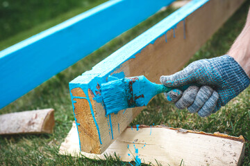 Hand painting wooden beam with blue paint outdoors showing diy renovation maintenance craftsmanship and home improvement process with copy space for construction repair and creative work concept