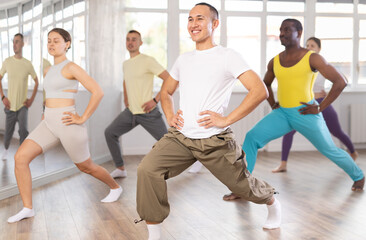 Obraz premium Active young Asian man doing leg exercises in training hall during dancing classes