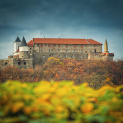 View to castle Palanok on hill through autumn leaves on foreground under cloudy sky in autumn day in Ukraine