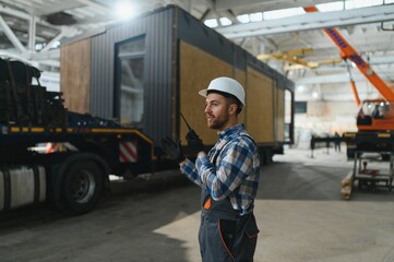 A worker controls the process of loading a modular house onto a truck. Transportation and delivery concept