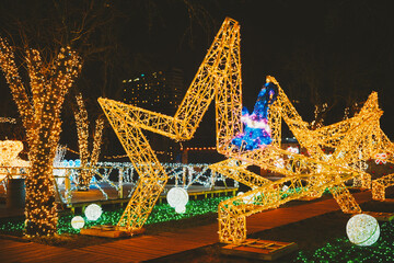 Elaborate golden star displays sparkling bright at night, trees wrapped in warm festive lights, green ground
