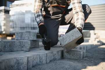 Close-up of construction worker installing and laying pavement stones on terrace, road or sidewalk. Worker using stones and rubber hammer to build stone sidewalk