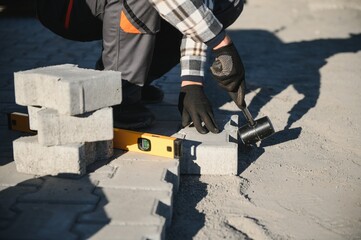 Builder laying a paving brick placing it on the sand foundation with gloved hands
