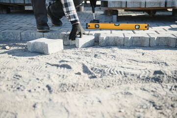 Close-up of construction worker installing and laying pavement stones on terrace, road or sidewalk....