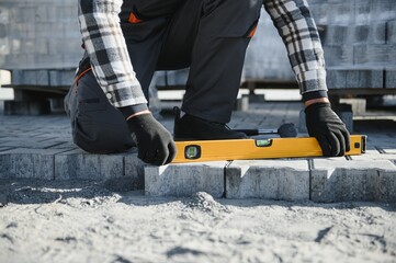 The master in gloves lays paving stones in layers. Garden brick pathway paving by professional...