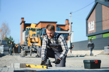 Builder laying a paving brick placing it on the sand foundation with gloved hands