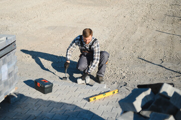 Construction worker installing and laying pavement stones on terrace, road or sidewalk. Worker...