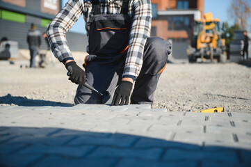 Builder laying a paving brick placing it on the sand foundation with gloved hands