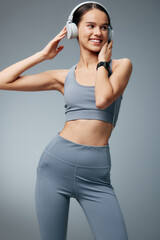 Obraz premium Fitness woman in athletic wear with headphones, smiling as she poses mid workout in a studio. A dynamic scene capturing energy, focus, music, and an active lifestyle.