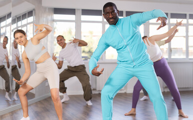 Positive Afroamerican guy engaged in breakdancing together with other attendees of dancing courses