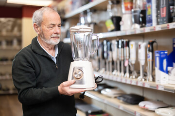 Senior man stands in a household appliance store and chooses a blender to make soups, purees and...