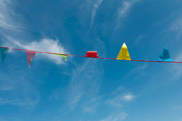 Bright pennant flags on red string against blue sky with clouds. Festive outdoor decoration for celebration and party events.