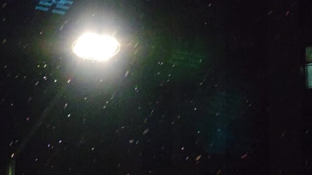 Snowfall under glowing streetlight at night