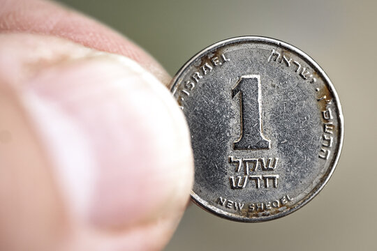 Macro close-up of an old rusty used Israeli one shekel coin held between fingers, showing metal texture, denomination, and national currency detail.