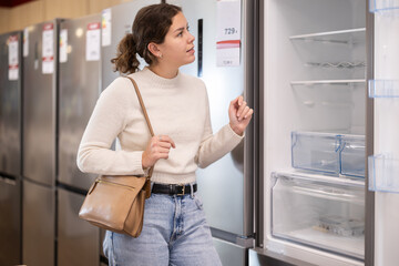 Young woman buyer chooses electric refrigerator in home appliance store