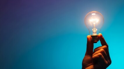 A hand holds a brightly glowing incandescent light bulb against a gradient background transitioning from dark blue to turquoise illuminating the fingers