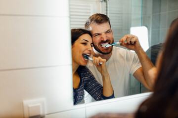 Young happy couple brushing teeth together in a modern bathroom. Morning routine and dental hygiene concept