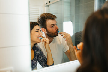 Young happy couple brushing teeth together in a modern bathroom. Morning routine and dental hygiene concept