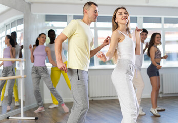 Naklejka premium Happy young woman and man with group of multinational people enjoying active boogie-woogie dance in modern studio. Social dancing concept