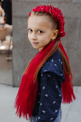 Child with bright red braided hairstyle featuring dual braided buns decorated with pearl beads, showcasing creative hair styling with synthetic extensions and playful expression indoors