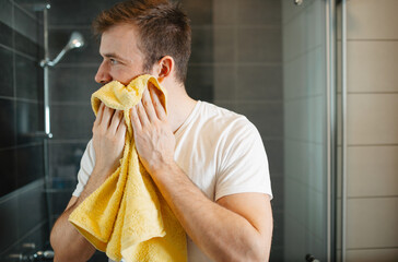 Man drying his face with a soft white towel in a modern bathroom. Morning grooming and hygiene routine

