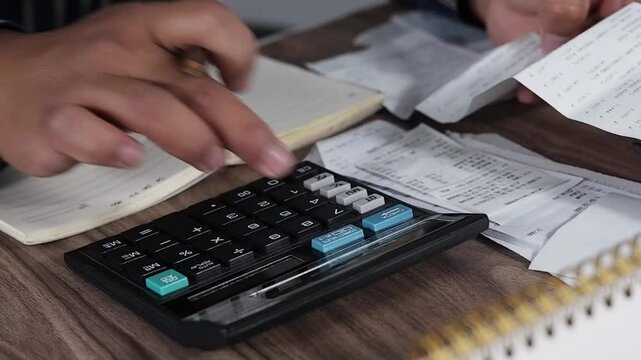 Close-up of a man's hands looking at a shopping receipt and calculating it with a calculator. Invoices, calculating household budgets, household expenses. Insurance or mortgages. Household financial m
