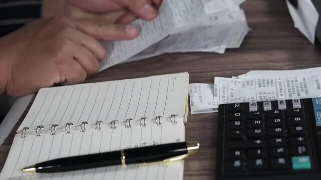 Double-checking the pile of notes or shopping receipts on the work desk.
A person reviews a stack of checks and paper receipts. Excessive, irrational, and reckless spending. Financial problems. Financ