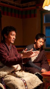 Tibetan Men in Traditional Robes Talking and Gesturing Inside Decorated Cultural Home