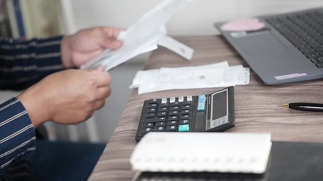Double-checking the pile of notes or shopping receipts on the work desk.
A person reviews a stack of checks and paper receipts. Excessive, irrational, and reckless spending. Financial problems. Financ