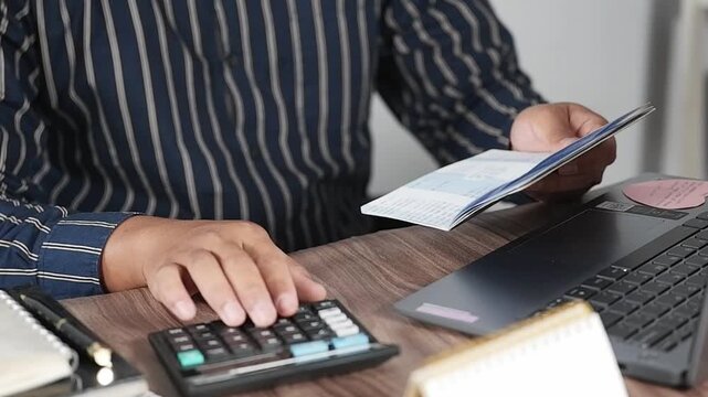 Open and check the printout of savings book, view bank account book in front of laptop, account statement, check payment and income, financial documents, pay slip, cash balance, investment, business.