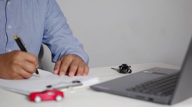 Car buying, selling, or leasing. A customer at a car showroom signs a paper after completing a loan application and financing documents. A customer at a dealership signs financial documents, camera cl