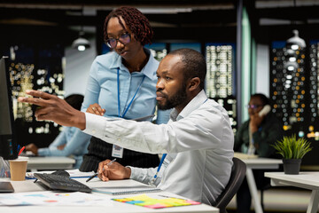 Fototapeta premium Black confident business partners in office at night analyzing metrics on desktop pc, focusing on report writing and planning to drive results and success. Doing overtime together.