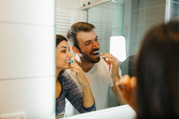 Young happy couple brushing teeth together in a modern bathroom. Morning routine and dental hygiene concept