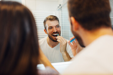 Handsome man cleaning teeth with a toothbrush looking in the mirror