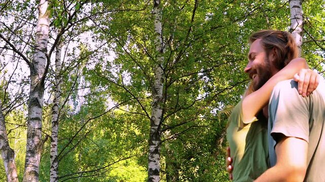 tender embrace of young loving couple outdoors in lush green summer forest man with long hair beard holding woman with reddish hair as she leans head on his chest both smiling gently eyes closed