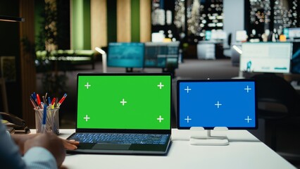 Black employee working with green screen and blue screen on laptop and tablet, engaged in budgeting or financial projections at night time. Businessman solving important tasks with gadgets.